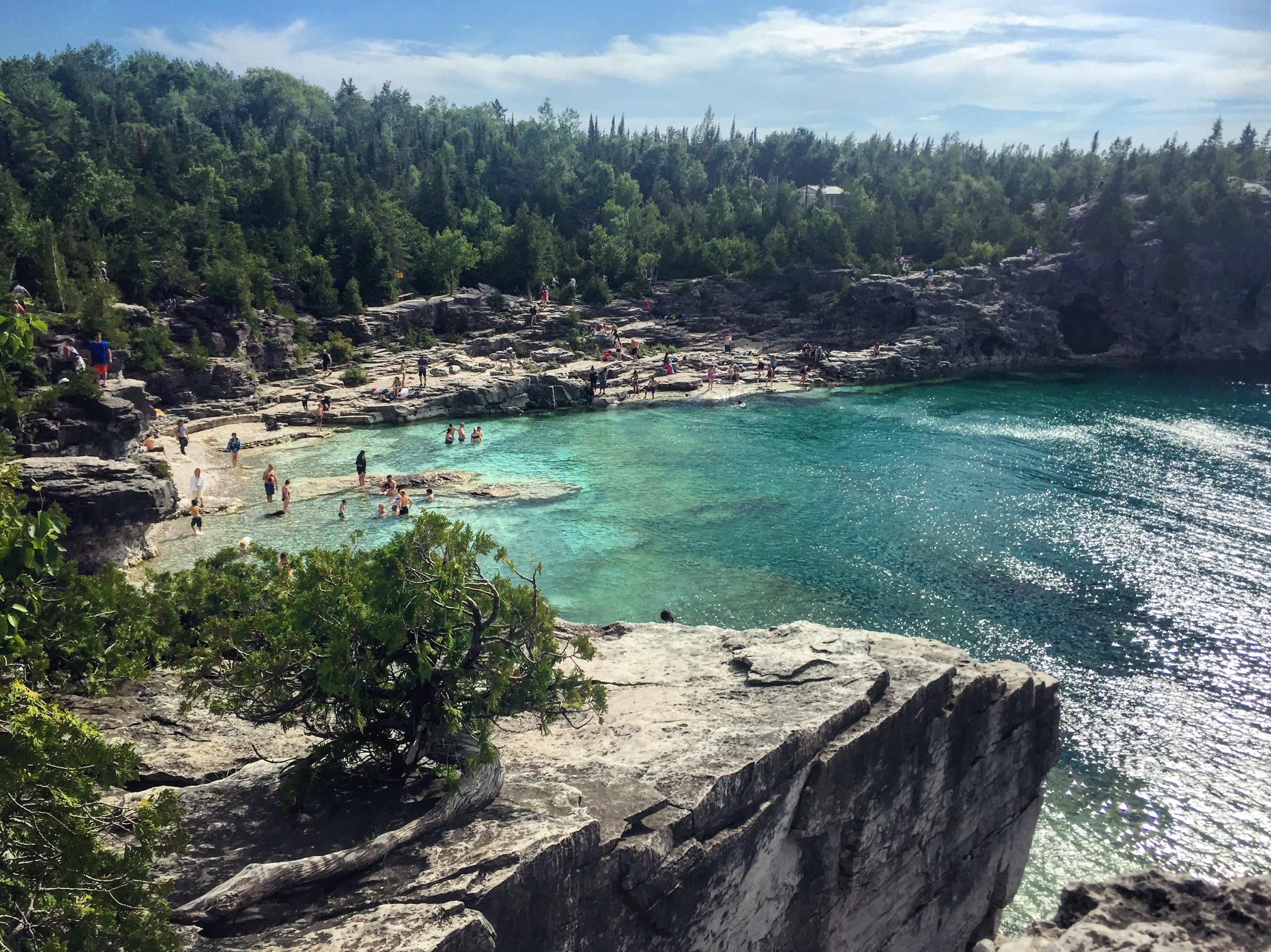 a cliff side with a body of water below with Bruce Peninsula National Park in the background